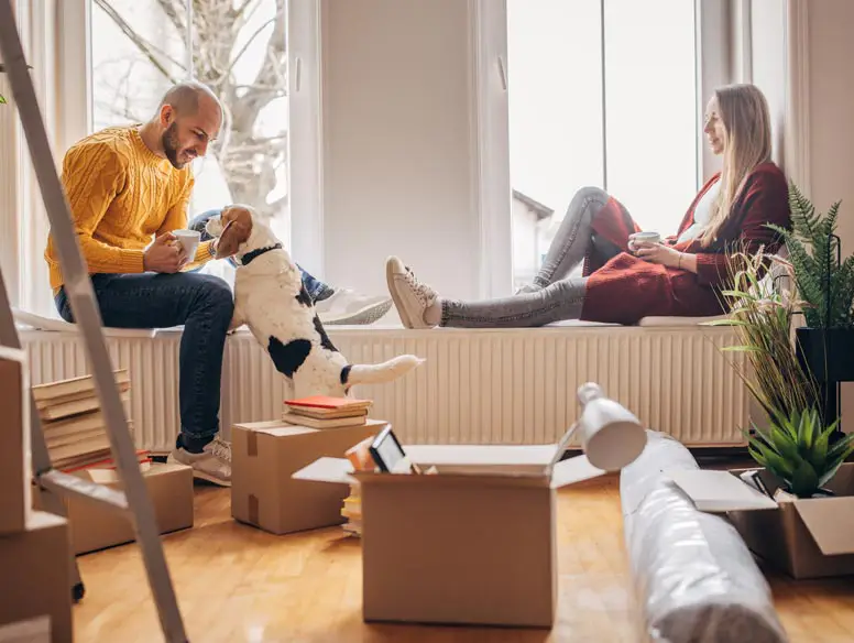 couple sitting in front of windows with their dog, surrounded by boxes. 