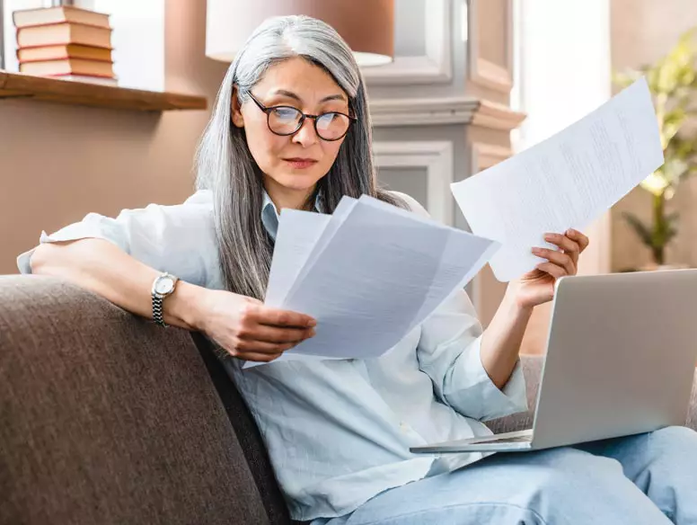 Woman looking over paperwork with laptop