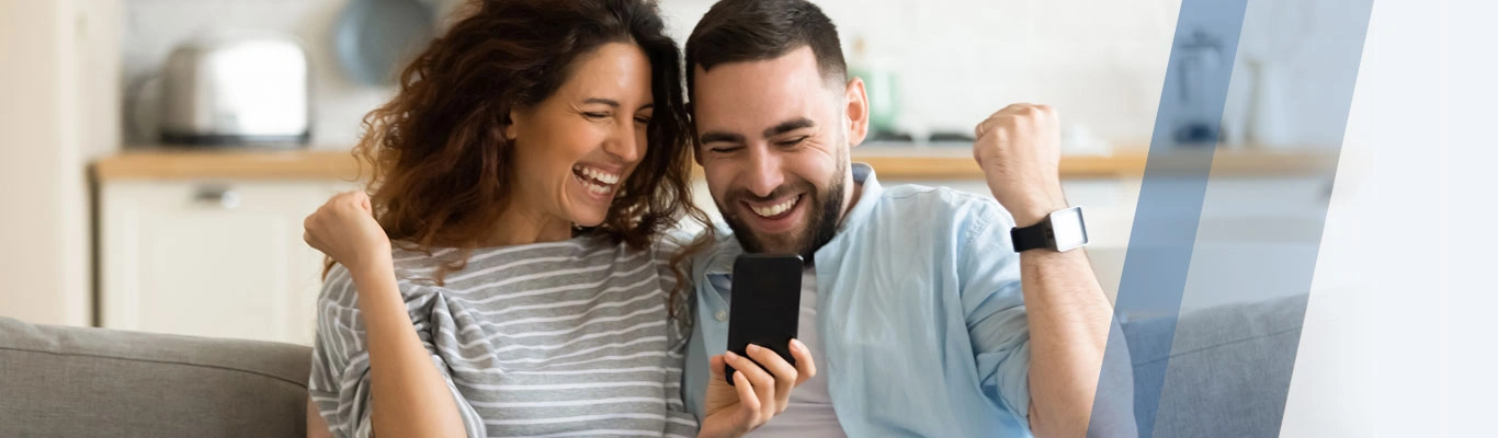 couple celebrating on couch looking at a phone.